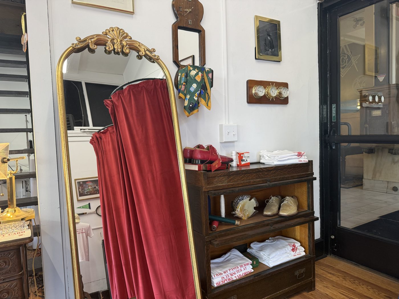 A gold-framed mirror, red velvet curtain and shelves of shoes and shirts