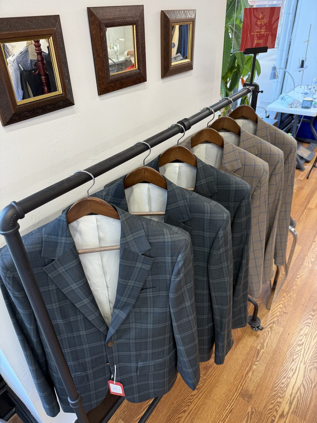 A rack of plaid and windowpane blazers on wooden hangers beside a Seasonal Blazers price sign